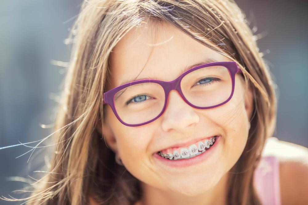 young girl with glasses smiling brightly with braces I jerger pediatric dentistry