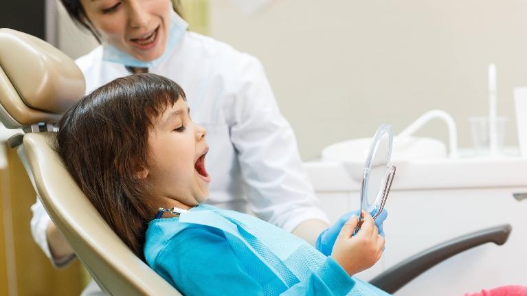 Young child looking at her teeth in the mirror after dental cleaning in Decatur, IL